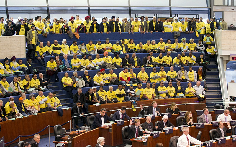 Демонстранты (в желтых футболках) слушают дебаты о внесении изменений в правила регулирования услуги такси в городском совете в Торонто, Канада, 30 сентября 2015 года. 
