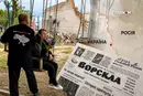 Наталія Пасюга з детектором дронів «Чуйка» на гойдалці в прифронтовому Спірному. Позаду – руїни кафе, де була точка розповсюдження газети «Ворскла» 