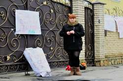 Активістка під стінами єпархії. На паркані висять плакати, на землі лежать іграшки та труна з написом: «Кубло російського окупанта» 